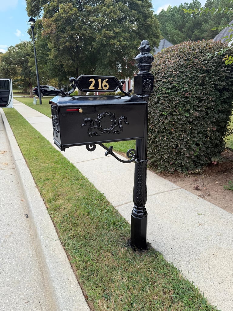 Black decorative mailbox with number 216 mounted on ornate post along suburban driveway with hedge